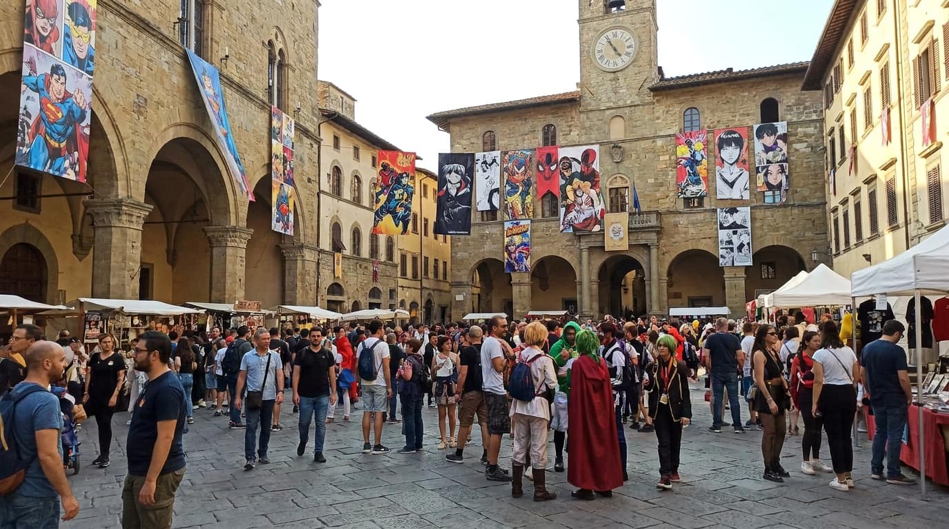 Piazza medievale italiana gremita di visitatori con stand e striscioni del festival fumetto